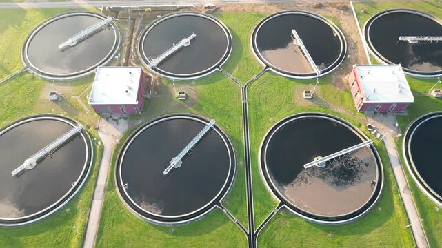 Aerial view of water treatment facility showcasing circular tanks and machinery. Sewerage system surrounded by greenery. Modern industrial plant of big city. Ecology friendly factory