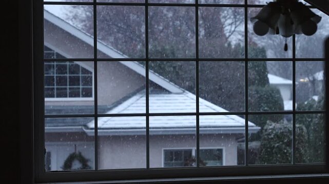 Early snow fall outside, from the point of view of inside a home with a big grid window. View of the neighbour's house along with Christmas wreaths. 