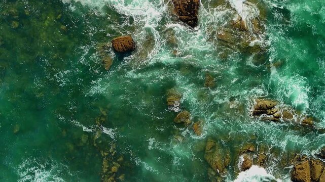 Drone gliding backward in bird&rsquo;s-eye view above darker greenish Atlantic ocean waves with muted silver sea foam and rocky coastal formations near &Acirc;ncora, Portugal