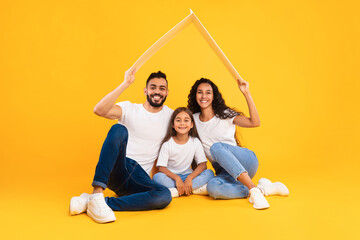 A joyful family sits together on the floor, with a young girl in the middle, holding a cardboard...