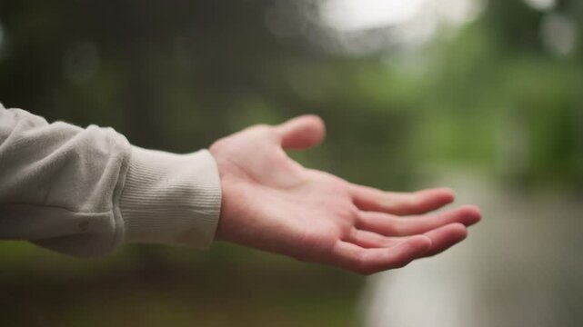Hand skillfully holding gentle raindrops, Calm scene with hand catching gentle rain in park setting, Serene atmosphere with outstretched hand floating amidst gentle rain in peaceful park