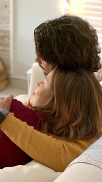 Vertical video: Settling couple in mustard sweater holding on couch for comfort, logs visible