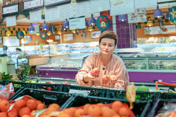 Obraz premium Middle-aged woman in pink suit choosing fruits and vegetables in a large shopping mall supermarket