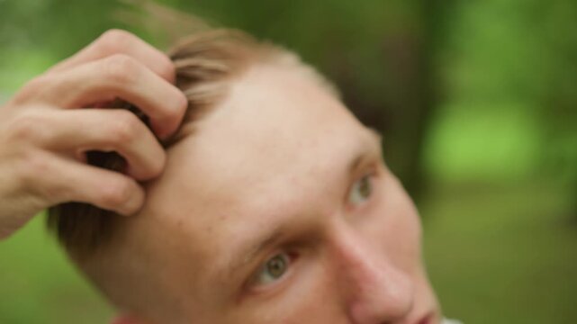 closeup white man styling wet hair in green park, combing defined part with fingers, neat fade and pomade sheen, focused gaze and precise hand movements, casual outdoor grooming scene