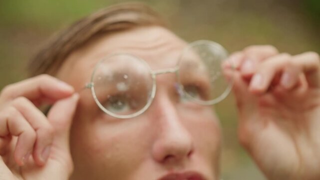 Young observer inspects treetops carefully, Caucasian youth adjusts glasses while viewing canopy, An observant young individual refreshes his vision and gazes upward into lush woodland canopy