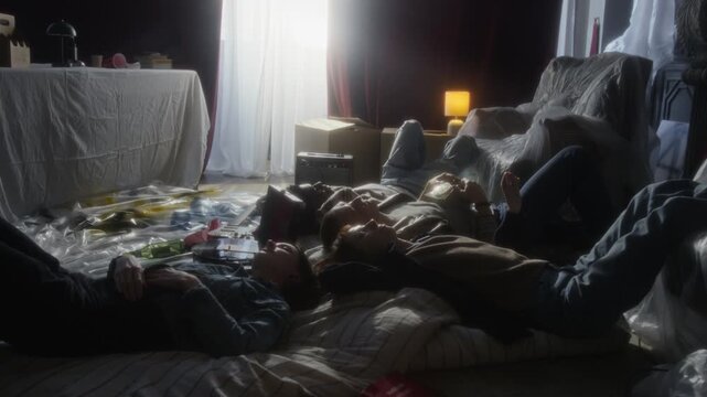 Side view zoom in shot group of young people lying on floor mattresses together while hanging out in abandoned house and listening to music, copy space