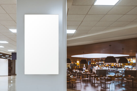 Vertical blank screen mockup on wall in modern cafe or food court interior, glowing display for advertising, clean design, large copy space area on right with soft background blur