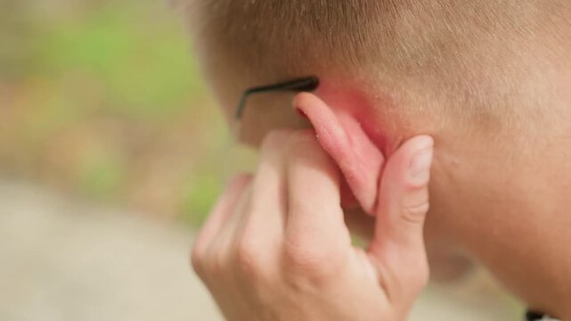 closeup man adjusting ear insert during walk on sidewalk, sweaty temple and glasses frame visible. fingertip presses soft insert into irritated ear, quick corrective motion against blurred park