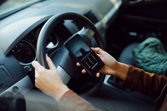 Fototapeta Close-up of a female driver using her smartphone behind the wheel.