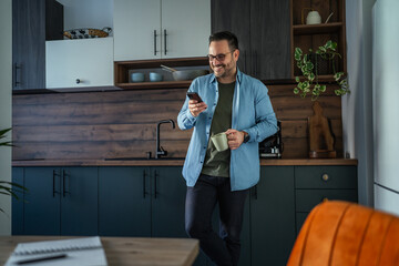 Man drinking coffee and checking phone in home office kitchen