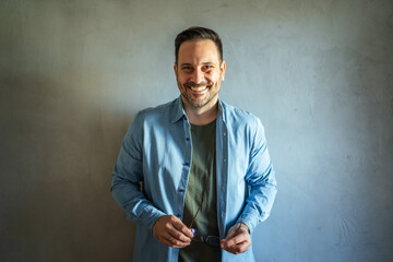 Smiling man holding glasses standing against wall
