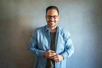 Smiling man wearing glasses standing against gray wall