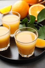 Fresh orange juice, fruits and leaves on grey table, closeup