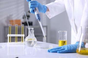 Scientist with dripping motor oil into Petri dish at table in laboratory, closeup