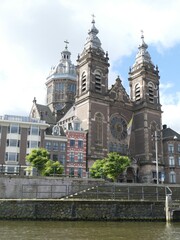 Naklejka premium Canal-side perspective revealing Saint Nicholas Basilica's ornate facade, architectural details framing historic Amsterdam urban landscape