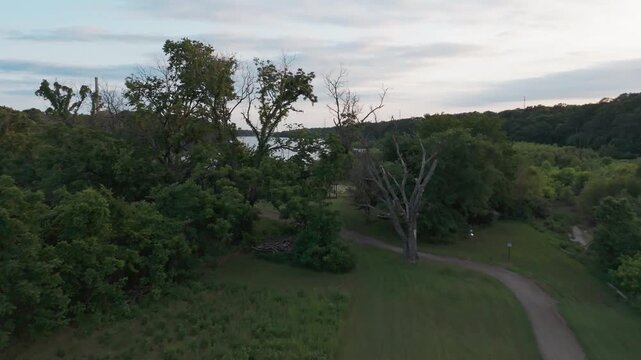 Aerial dolly along winding forest path approaching sandy lake edge, overview with power plant
