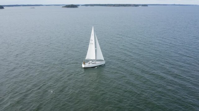 Sailboat navigating with full sails in Finland South West archipelago. Small islands in the background. Aerial drone side view.