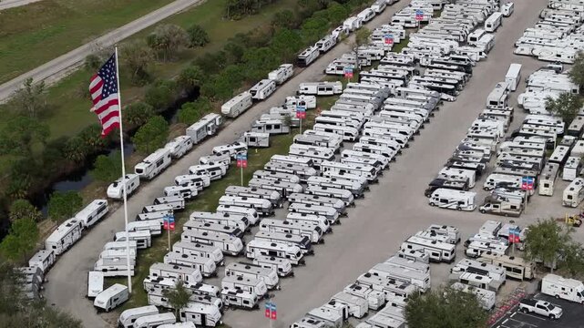 Large parking lot of local dealer with many new RV trailers parked for sale. Distribution of manufactured camping vehicles.