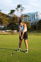 Latin hispanic woman golfer dressed in sportswear focusing on teeing off, concentrating intently on her golf swing on a green course