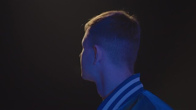 young caucasian man under streetlight, varsity jacket lit by blue rim light, profile shifts from shadow to face, driver checking route, latenight commuter pausing at curb, lookout scanning distant