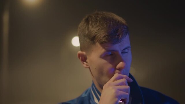 closeup night portrait white man vaping under soft streetlight bokeh, blue varsity jacket, exhaled vapor curling through mist, introspective mood, latenight driver daydream and anonymous urban