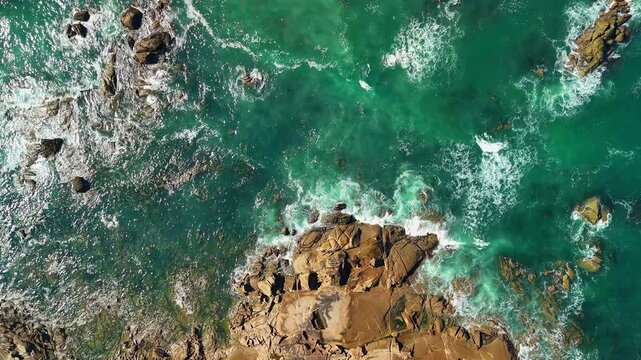 Aerial drone hovering above ocean waves near a rocky coastline in &Acirc;ncora, Portugal, capturing textured water movement, white foam patterns, and rugged Atlantic coastal scenery