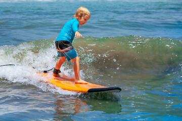 Happy young surfer boy with surfboard have fun on beach, riding on small ocean waves. Summer adventures, active families, parents and kids lifestyle, sports activities on school holiday with kids