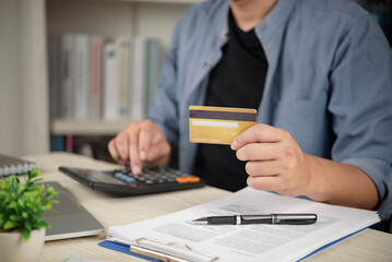 Man holding credit card and using calculator for financial planning, paying bills, checking debt balance, and online shopping at home office desk.