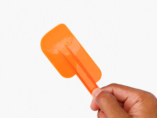 A closeup image of a hand holding a flat plastic kitchen spoon on a clean white background, commonly used for spreading butter, scooping ground spices, and general cooking preparation.