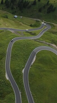 Vertical screen Aerial view two lane mountain road weaving through green slopes, solo motorcyclist touring scenic switchbacks while drone films panoramic alpine landscape.