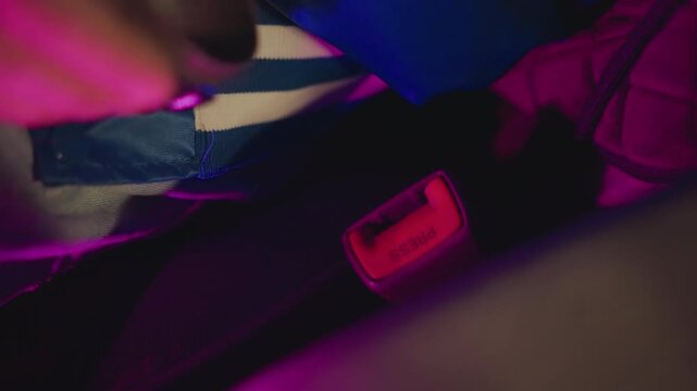 driver hand fastening pink buckle under neon glow, closeup belt click before night departure, textured upholstery and dashboard lights, urban commute precaution, calm focused motion