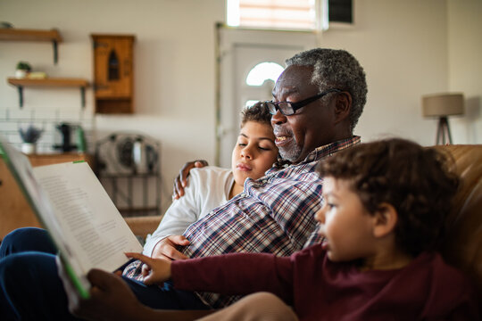 Senior grandfather lovingly reading with young grandsons on cozy living room sofa