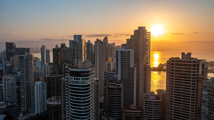 Obraz premium Stunning aerial view of Panama City skyscrapers with golden sunrise light reflecting brightly off the ocean water