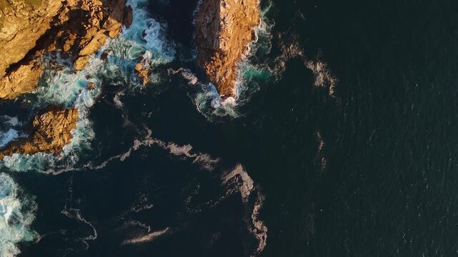 Aerial drone flying forward birds-eye view above O Berron Da Nave rock island with ocean waves and birds in Spain