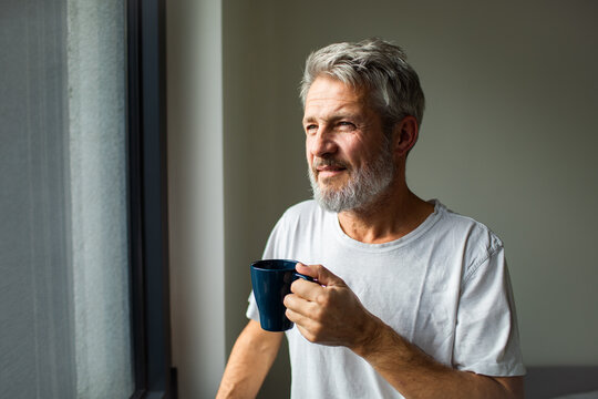 Mature man sipping coffee by window at home, calm and thoughtful