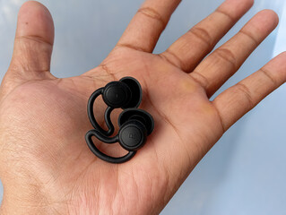 Black silicone ear plugs held on an open hand against a clean background, designed to reduce noise, protect ears, and provide comfort for daily use or rest.