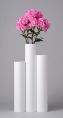 Fototapeta premium Pink flowers bloom in a trio of white cylindrical vases.