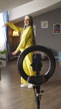 Young woman in hijab recording dance video on tripod smartphone wearing yellow suit showing influencer lifestyle creative content production social media trend joyful movement and modern digital