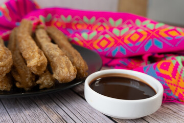 Close-up of churros with chocolate on a table and a Mexican tribal fabric