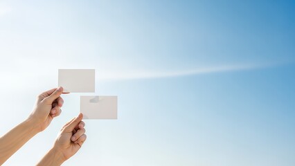 Hands Holding Two Blank White Cards Against a Clear Blue Sky, Copy Space for Messages.