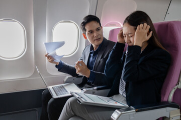 Two Asian business professionals in a heated discussion during a flight. man points at documents...
