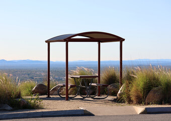Picnic table under a curved roof gazebo surrounded by rocks and long grass at the Towers Hill Lookout in Charters Towers, Queensland, Australia