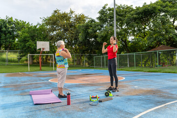 Senior woman doing bicep curls with dumbbells under supervision of female personal trainer outdoors