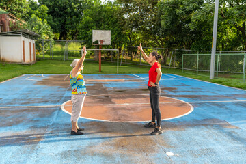 Senior woman and female personal trainer doing stretching exercises on an outdoor basketball court
