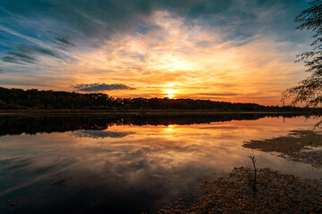 Beautiful summer sunset and colorful sky over the lake. Clouds are reflected in the calm water. Beauty in this world