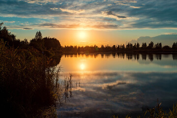Beautiful summer sunset and colorful sky over the lake. Clouds are reflected in the calm water. Beauty in this world