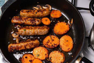 Cooking sausages and sweet potatoes in a frying pan on a kitchen stove in the evening meal preparation