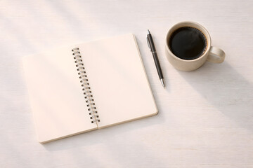 Minimal workspace flat lay with blank notebook, pen, and coffee cup on white wooden desk, copy space for text