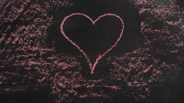 A hand draws a pink heart on a dark blackboard. It is suitable for Valentine's Day celebrations and general love relationship themes in digital content.