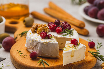 Brie cheese on a board with walnuts, honey and berries